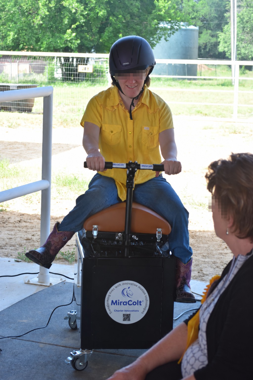 A helmeted participant in a yellow shirt seated on the MiraColt™ with a person alongside.