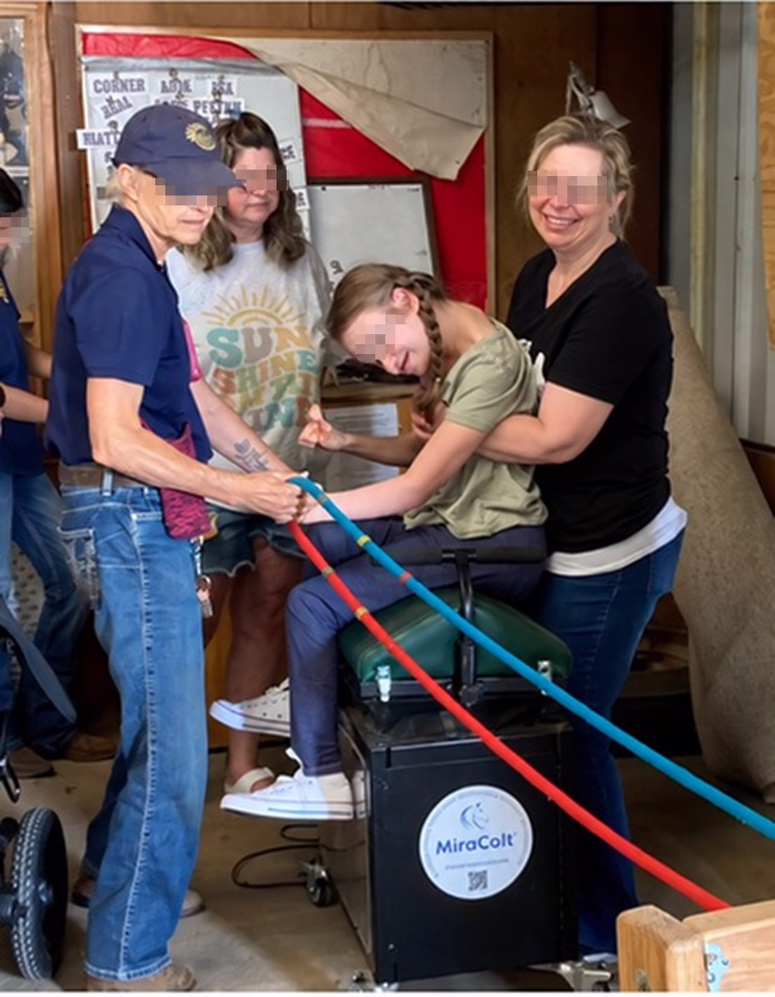 A participant seated on the MiraColt™ with adults providing support alongside.