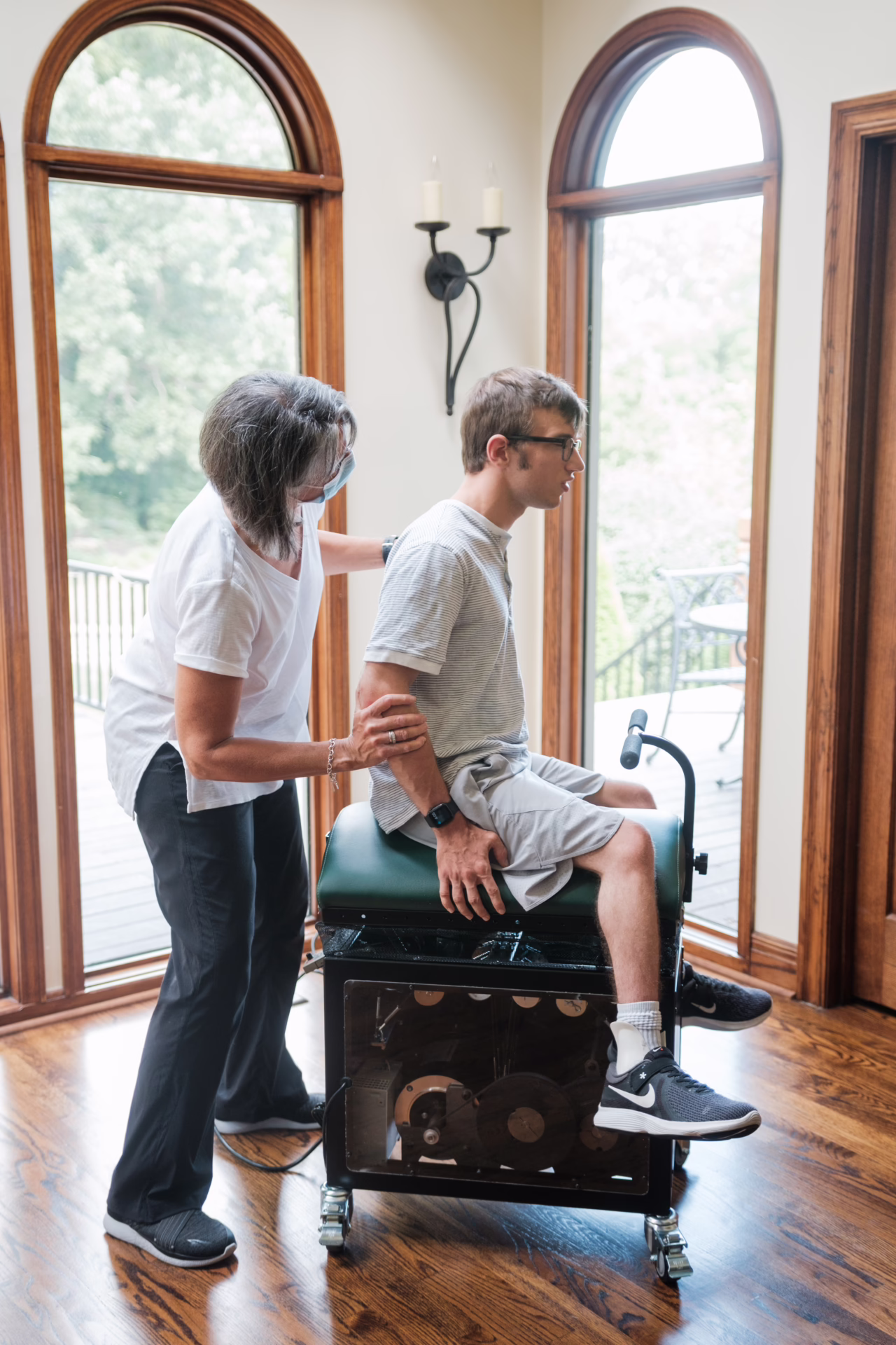 Joe sitting upright on the MiraColt while a person supports his arm and back.